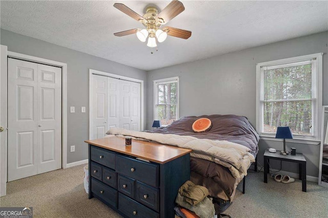 carpeted bedroom with ceiling fan, a textured ceiling, and two closets