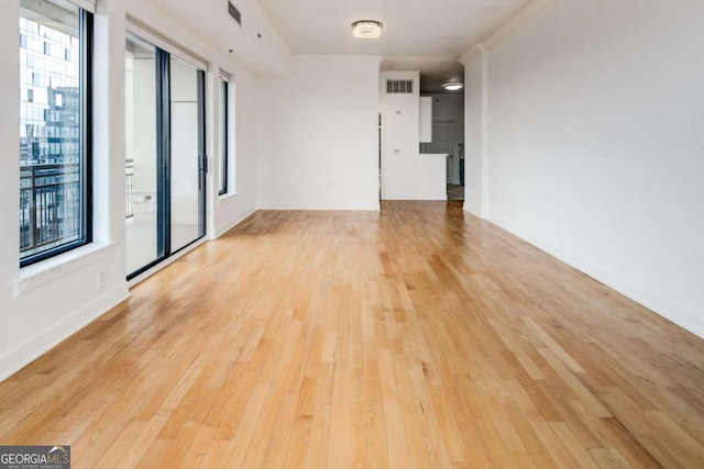 empty room with light wood-type flooring, visible vents, and crown molding