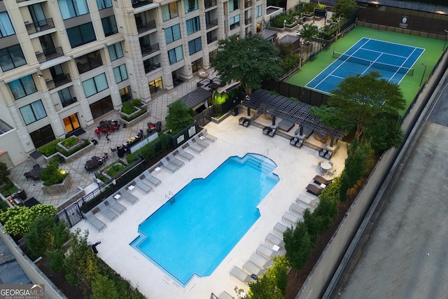 community pool with a tennis court, fence, and a patio