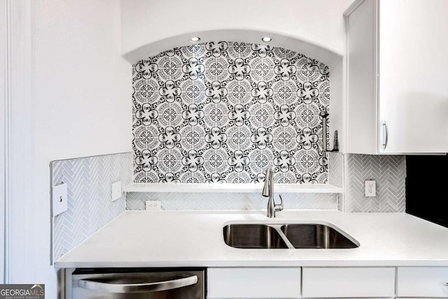 kitchen with decorative backsplash, light countertops, stainless steel dishwasher, white cabinetry, and a sink