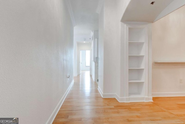 hallway featuring baseboards, light wood-type flooring, and crown molding