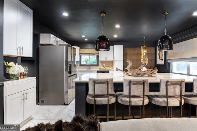 kitchen featuring stainless steel refrigerator with ice dispenser, a kitchen bar, light stone counters, a kitchen island, and white cabinets