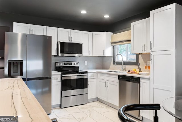 kitchen with sink, backsplash, stainless steel appliances, light stone countertops, and white cabinets