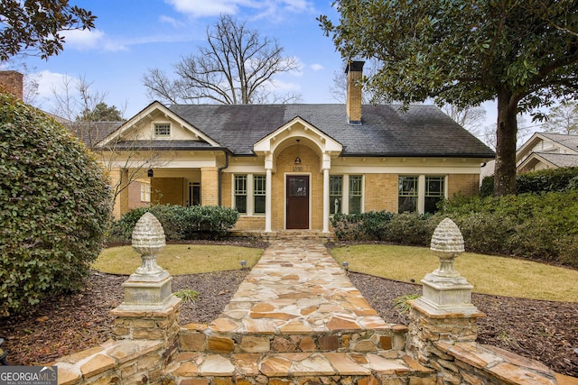 view of front of home featuring brick siding, a chimney, a front yard, and roof with shingles