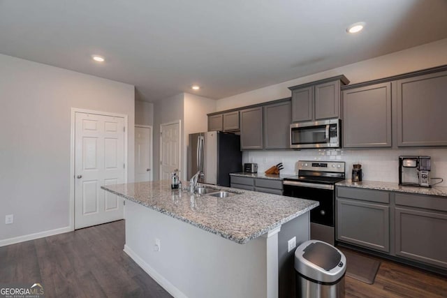 kitchen featuring sink, gray cabinetry, stainless steel appliances, light stone countertops, and a center island with sink