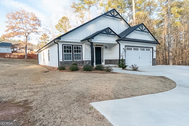 view of front of property with concrete driveway, an attached garage, board and batten siding, fence, and stone siding