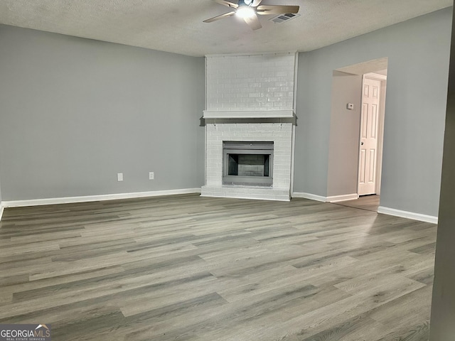 unfurnished living room with hardwood / wood-style floors, a fireplace, a textured ceiling, and ceiling fan