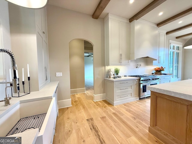 kitchen featuring arched walkways, range with two ovens, white cabinetry, light countertops, and wall chimney range hood