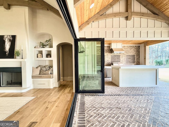 interior space featuring arched walkways, built in shelves, light wood-style flooring, a fireplace, and beam ceiling