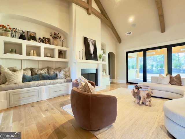 living area featuring high vaulted ceiling, built in shelves, light wood-style flooring, visible vents, and beam ceiling