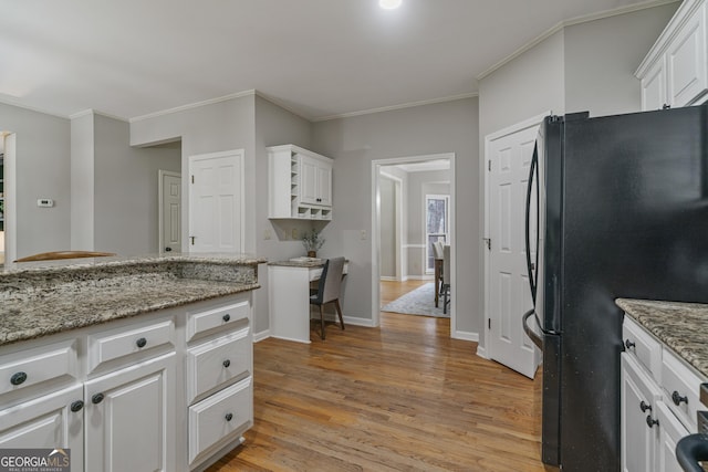 kitchen with light stone counters, freestanding refrigerator, white cabinets, and light wood-style floors