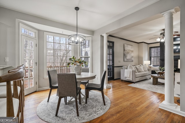 dining space with decorative columns, light wood-style flooring, ornamental molding, a ceiling fan, and baseboards