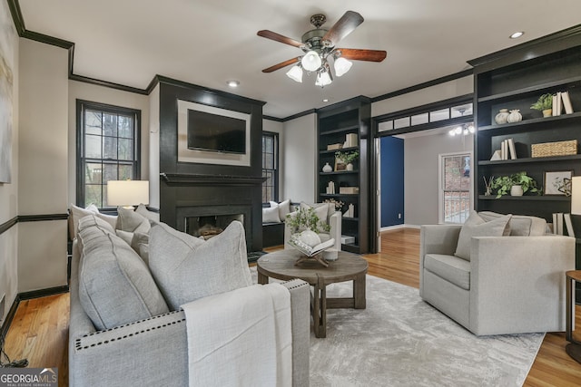 living area featuring a large fireplace, baseboards, ornamental molding, and wood finished floors