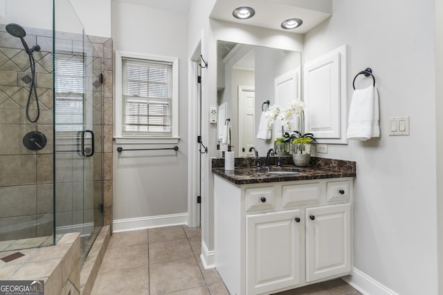 bathroom with a tile shower, tile patterned floors, vanity, and baseboards