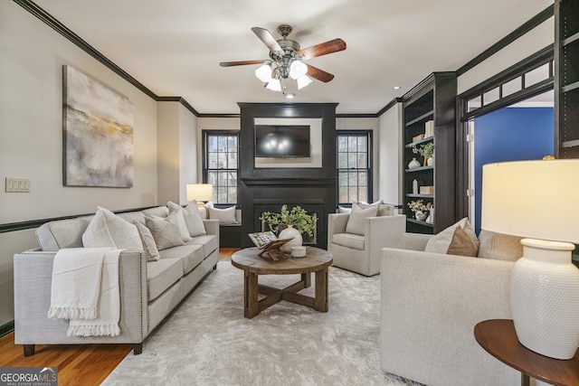 living area with a large fireplace, a ceiling fan, ornamental molding, and wood finished floors