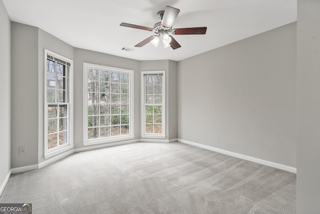 empty room featuring a ceiling fan, light colored carpet, visible vents, and baseboards