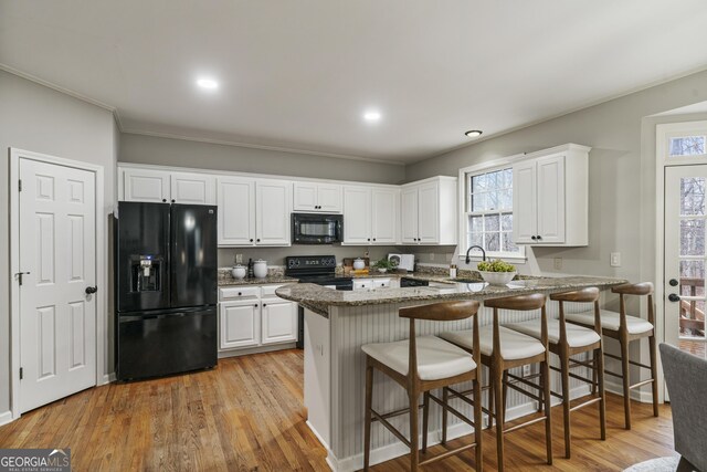 kitchen with dark stone countertops, white cabinets, a peninsula, and black appliances