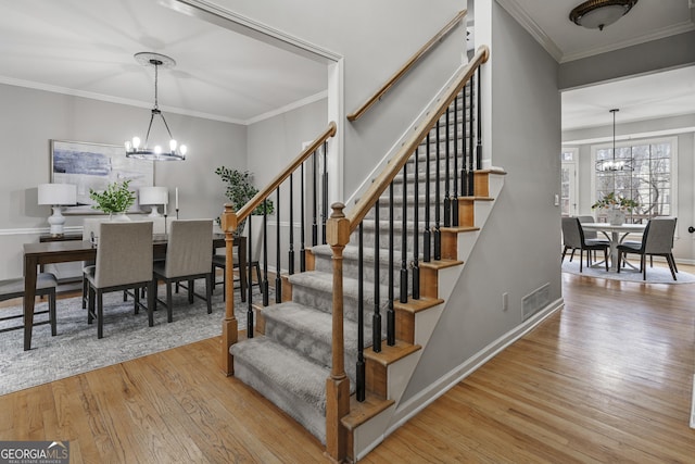 staircase featuring a chandelier, wood finished floors, visible vents, baseboards, and ornamental molding