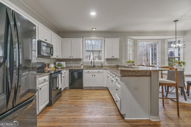 kitchen featuring dark stone countertops, decorative light fixtures, a peninsula, black appliances, and white cabinetry