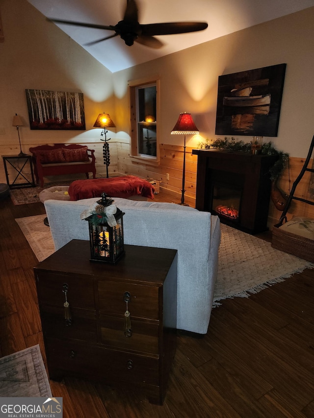 living room featuring vaulted ceiling, a lit fireplace, wood finished floors, and a ceiling fan