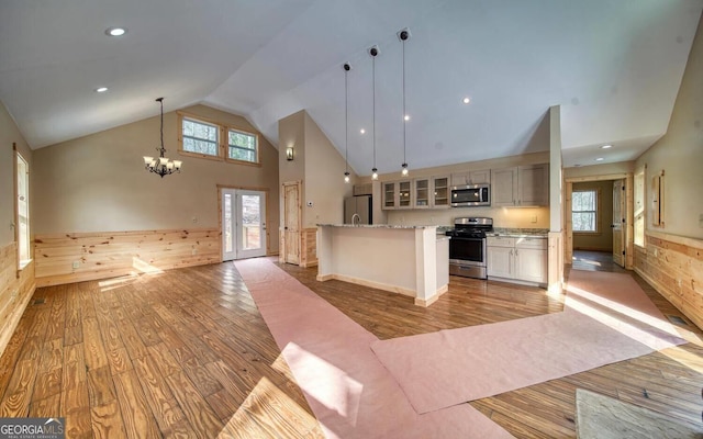 kitchen with pendant lighting, appliances with stainless steel finishes, high vaulted ceiling, light hardwood / wood-style floors, and a kitchen island