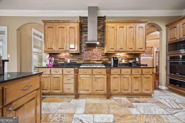 kitchen featuring dark stone countertops, appliances with stainless steel finishes, tasteful backsplash, and wall chimney range hood