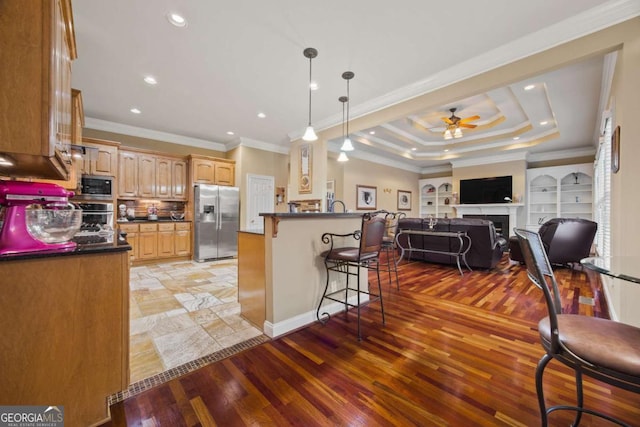 kitchen featuring light wood-type flooring, appliances with stainless steel finishes, a tray ceiling, pendant lighting, and ceiling fan