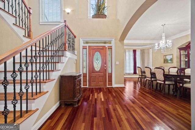 entrance foyer with a high ceiling, ornamental molding, a notable chandelier, and dark hardwood / wood-style flooring