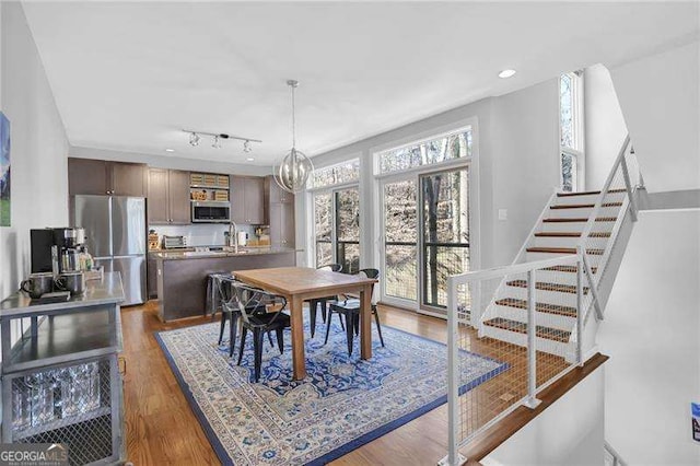 dining area featuring rail lighting, sink, an inviting chandelier, and dark hardwood / wood-style flooring