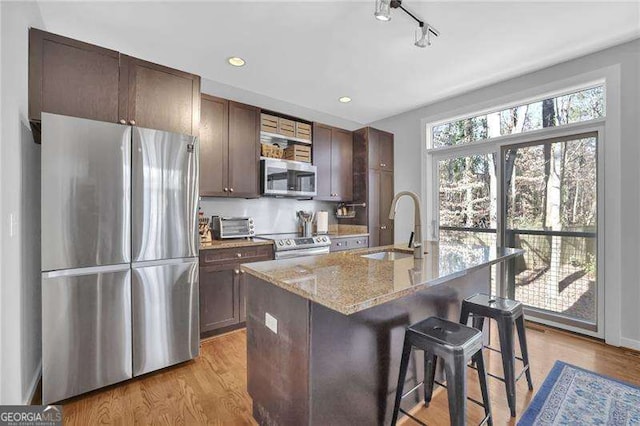 kitchen with sink, a breakfast bar area, light stone counters, an island with sink, and stainless steel appliances