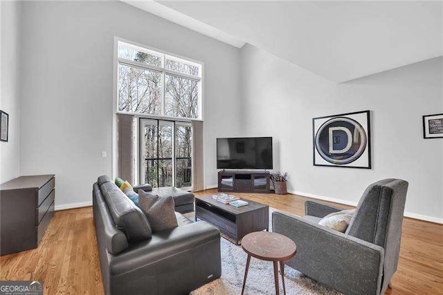 living room with a high ceiling, plenty of natural light, and light hardwood / wood-style flooring