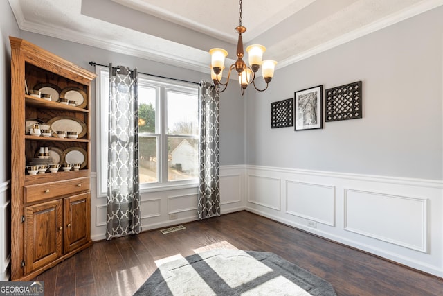 unfurnished dining area featuring a raised ceiling, ornamental molding, dark wood-type flooring, and a chandelier