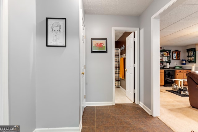 hallway with wine cooler, a textured ceiling, and dark colored carpet