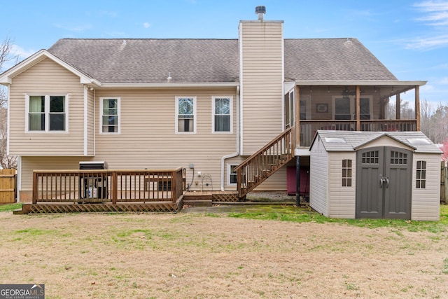 back of property with a wooden deck, a storage unit, a sunroom, and a lawn