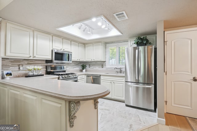 kitchen featuring appliances with stainless steel finishes, sink, white cabinets, kitchen peninsula, and a textured ceiling