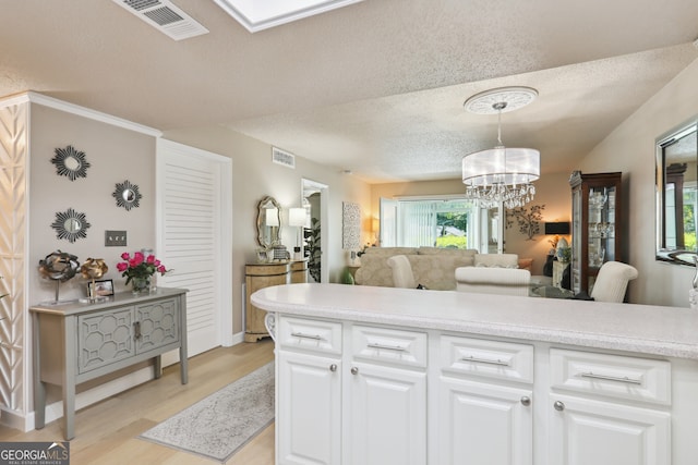 kitchen featuring light hardwood / wood-style flooring, hanging light fixtures, a textured ceiling, white cabinets, and a chandelier