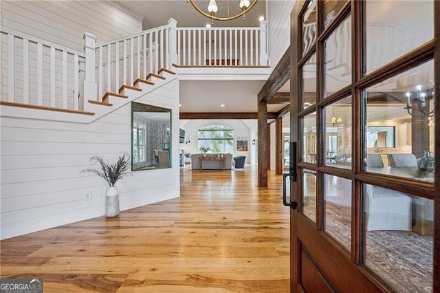 foyer entrance featuring an inviting chandelier, hardwood / wood-style floors, wood walls, and a high ceiling