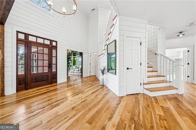 entrance foyer featuring a towering ceiling, wood walls, hardwood / wood-style floors, and a notable chandelier