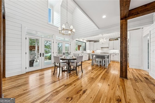 dining space with french doors, a chandelier, high vaulted ceiling, wooden walls, and light hardwood / wood-style floors