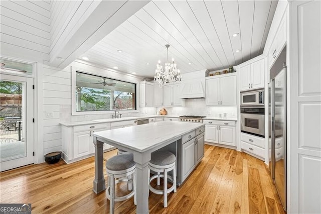 kitchen with appliances with stainless steel finishes, a center island, white cabinets, a kitchen bar, and custom exhaust hood