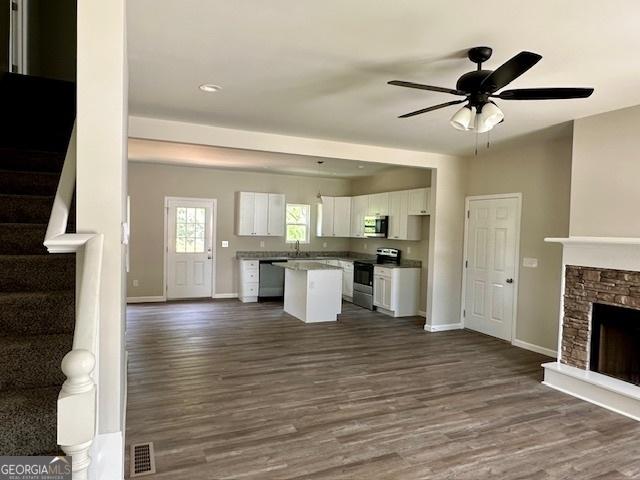 unfurnished living room with sink, a stone fireplace, dark hardwood / wood-style floors, and ceiling fan