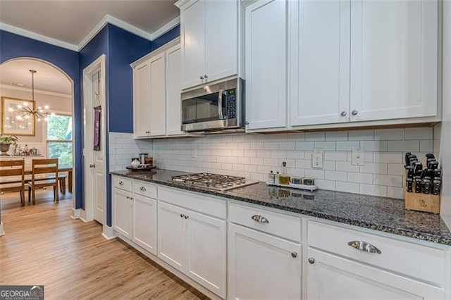 kitchen with an inviting chandelier, ornamental molding, light wood-type flooring, white cabinetry, and stainless steel appliances