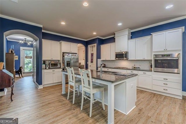 kitchen with crown molding, arched walkways, light wood-style flooring, and appliances with stainless steel finishes
