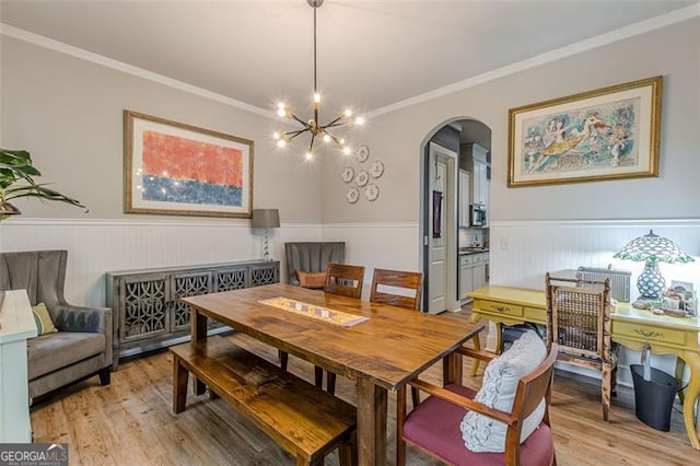 dining room featuring arched walkways, an inviting chandelier, wainscoting, and light wood finished floors