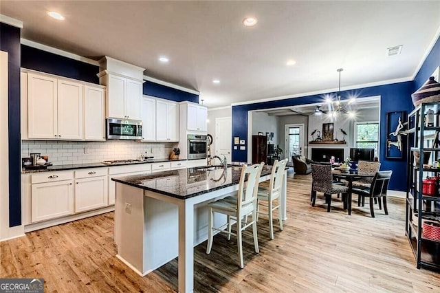 kitchen featuring tasteful backsplash, white cabinets, ornamental molding, stainless steel appliances, and light wood-style flooring