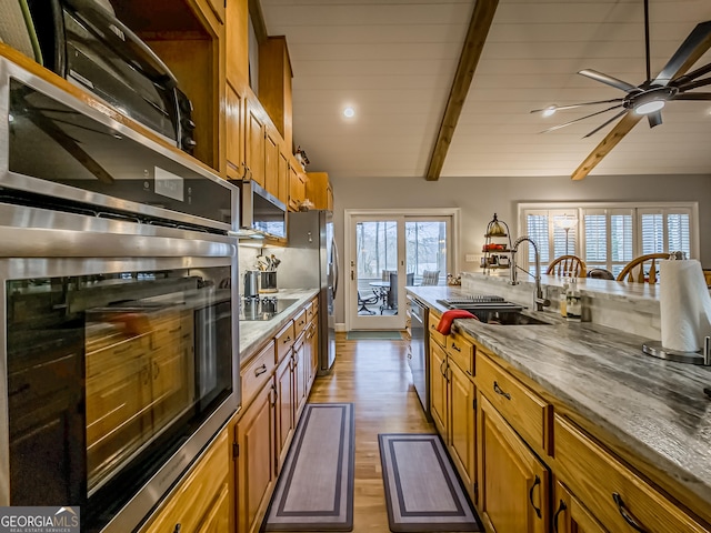 kitchen featuring appliances with stainless steel finishes, lofted ceiling with beams, ceiling fan, light hardwood / wood-style floors, and sink