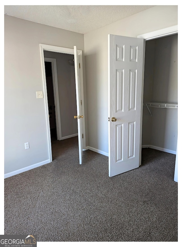 unfurnished bedroom featuring a closet, a textured ceiling, and dark colored carpet