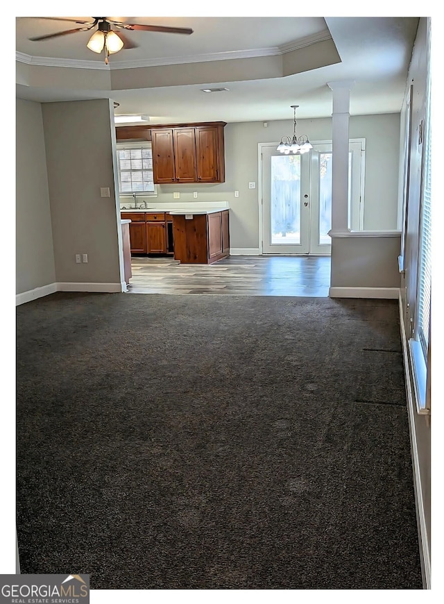 unfurnished living room with sink, ceiling fan, dark carpet, a raised ceiling, and crown molding