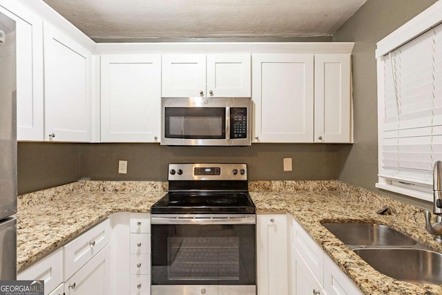 kitchen featuring sink, light stone counters, a textured ceiling, stainless steel appliances, and white cabinets