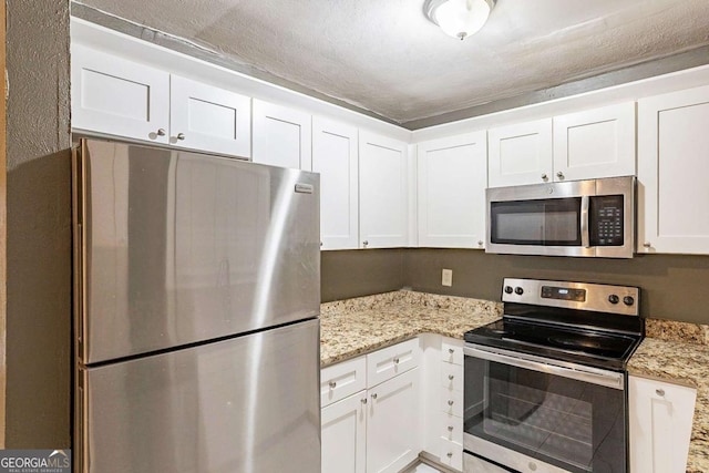 kitchen featuring appliances with stainless steel finishes, light stone countertops, a textured ceiling, and white cabinets